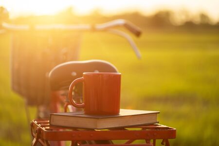Coffee cup put on the Red Japan style classic bicycle at view of green rice field in sunset timeの写真素材
