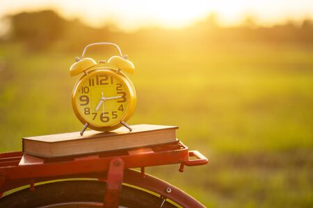 Yellow alarm clock and book put on the Red Japan style classic bicycle at view of green rice field in sunset timeの写真素材