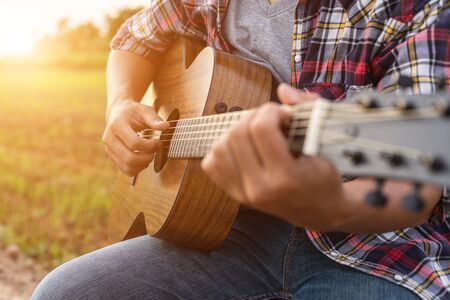 Asian man playing guitar at the green rice field in the sunset time. Countryside of Thailandの写真素材