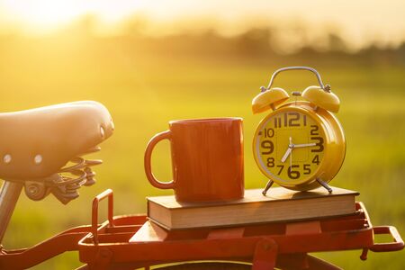 Coffee cup, clock, and book put on the Red Japan style classic bicycle at view of green rice field in sunset timeの写真素材