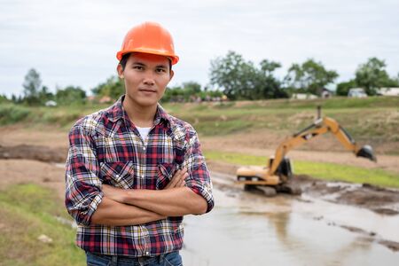 Asian young engineer working on site at the dam and control while excavator digging the earthの写真素材