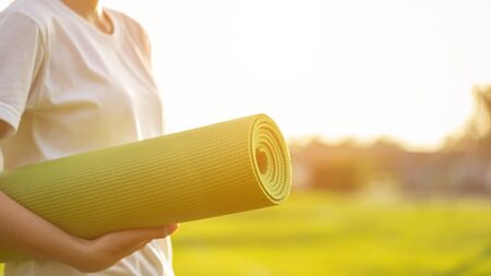 Pretty asian holding green yoga mat and prepare for doing yoga exercises in the park. Used for relax and healthy conceptの写真素材