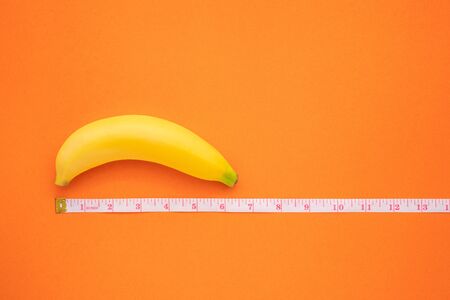 Close up yellow banana with measurement tape on orange background. Men penis size concept with empty free space for text or design. Top viewの写真素材