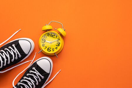 Top view new black fashion shoe and alarm clock on orange paper background. Copy space for text or...