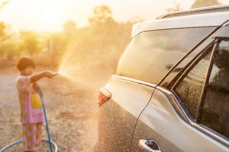 Happy asian little girl playing water from hose and spray to washing the car at outdoor in morning time. Kid and family activity conceptの写真素材