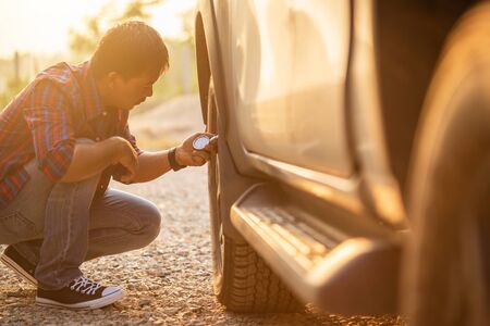 Asian man checking air pressure and filling air in the tires of his car. Car maintenance before driving conceptの写真素材