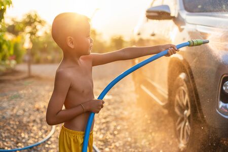 Happy asian little boy playing water from hose and spray to washing the car at outdoor in morning time. Kid and family activity conceptの写真素材