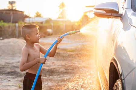 Happy asian little boy playing water from hose and spray to washing the car at outdoor in morning time. Kid and family activity conceptの写真素材