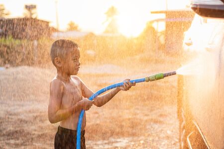 Happy asian little boy playing water from hose and spray to washing the car at outdoor in morning time. Kid and family activity conceptの写真素材