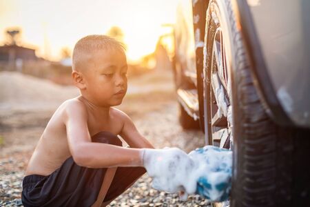 Happy asian little boy playing white soap and using blue sponge to washing the car at outdoor in sunset time. Kid and family activity conceptの写真素材
