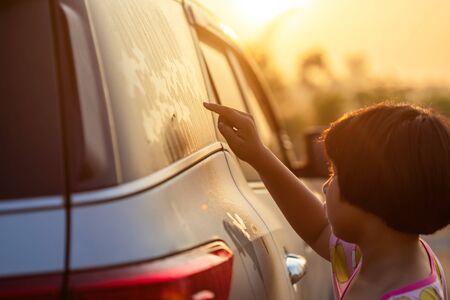 Asian little girl writing or drawing star symbol on wet mirror of her father SUV car in morning for love conceptの写真素材