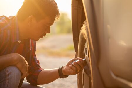 Asian man checking air pressure and filling air in the tires of his car. Car maintenance before driving conceptの写真素材