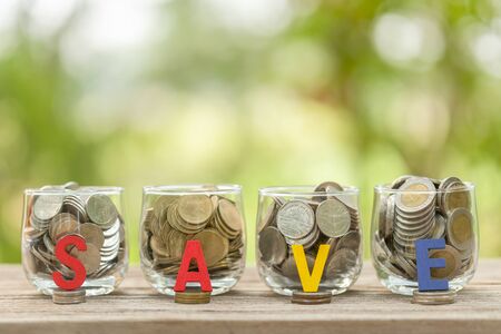 Close up coins in clear money jar on wooden table with green blur lightの写真素材