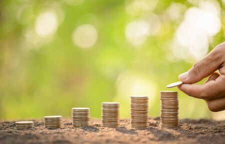 Close up hand putting coins in stack on wooden plank with green blur