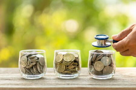 Close up blue stethoscope and jar of coin on wooden table. Money and financial checking conceptの写真素材