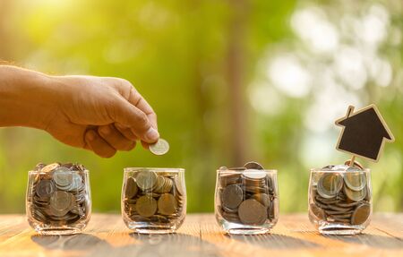 Close up hand put coin in clear jar on wooden table.の写真素材