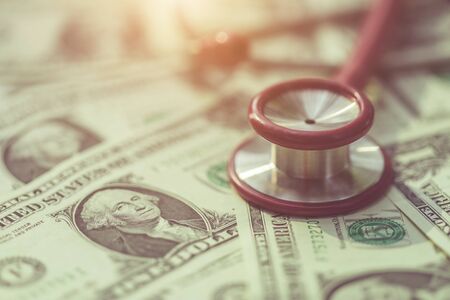 Close up red stethoscope on the US dollar banknote on wooden table. Health check or money and financial conceptの写真素材