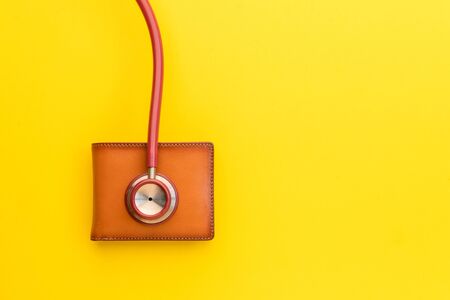 Close up doctor stethoscope and the new leather brown men wallet on yellow background. Budget for...