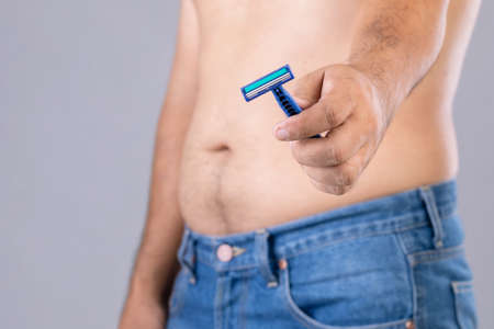 Portrait man using razor blade to cutting belly and body hair. Studio shot on grey backgroundの写真素材