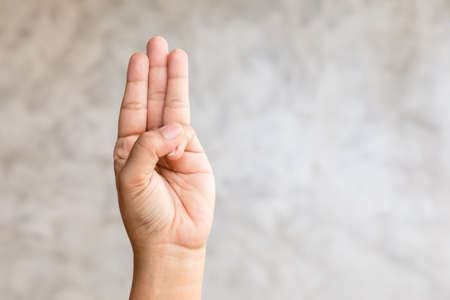 Close up hand showing three finger symbol on grey background with copy spaceの写真素材