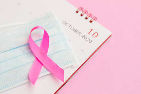 Breast Cancer concept : Top view pink ribbon, protective mask and calendar symbol of breast cancer campaign on pink backgroundの写真素材