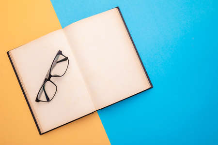 Top view new eyeglasses and book on yellow and blue background. Copy space for text or designの写真素材