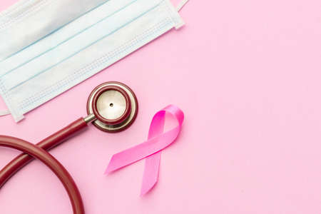 Breast Cancer concept : Top view pink ribbon, red stethoscope and protective mask symbol of breast cancer campaign on pink backgroundの写真素材