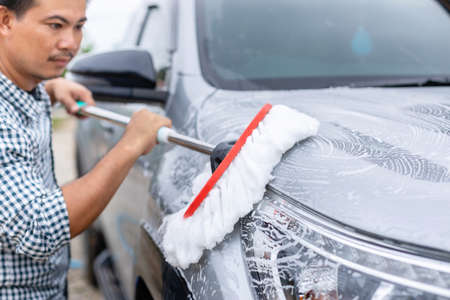 Asian man using white mop with soap to washing the car at outdoor. Car cleaning and maintenance conceptの写真素材