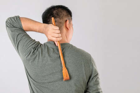 Health care or Itchy or Tinea Cruris concept : Portrait of people using Scratching wood stick to Scratch on his back side. Studio shot on grey backgroundの写真素材
