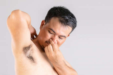 Bad smell underarm rash : Man checking and smelling his armpit. Studio shot isolated on grey backgroundの写真素材