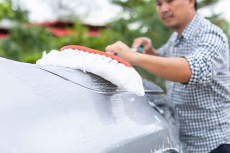 Asian man using white mop with soap to washing the car at outdoor. Car cleaning and maintenance conceptの写真素材