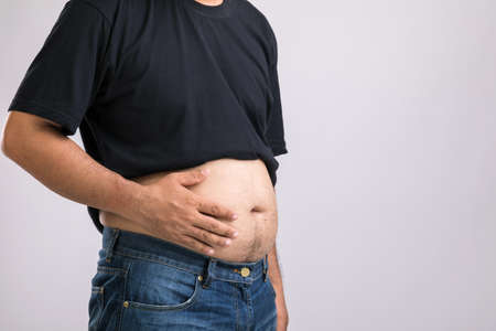Medical check up concept : Fat people showing his big belly. Used for liver problem or Obesity concept. Studio shot on grey backgroundの写真素材