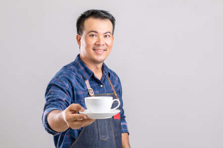 Portrait Asian man in barista uniform holding white coffee cup isolated on grey backgroundの写真素材