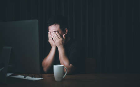 Eyestrain concept. Man touching his eyes because tired after working long time on computer. Dark...