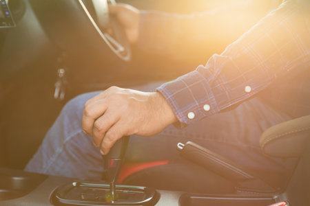 Car driving concept : Close up driver hand on automatic gear inside the modern car. Car interior with morning golden sun light flare effect. Transportation useの写真素材