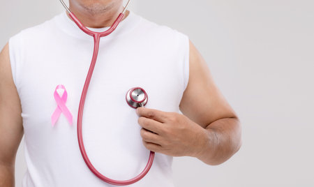 Breast cancer in men concept : Portrait Asian man holding stethoscope and pink ribbon the symbol of breast cancer campaign. Studio shot isolated on grey backgroundの写真素材