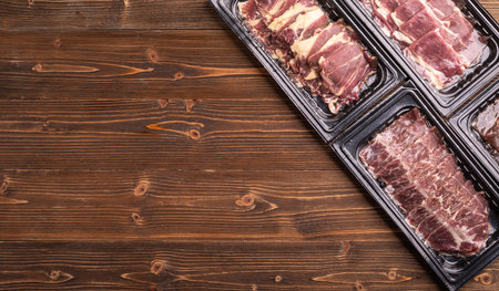 Top view pack of raw sliced Dry Aged beef in black plastic tray on wooden table background