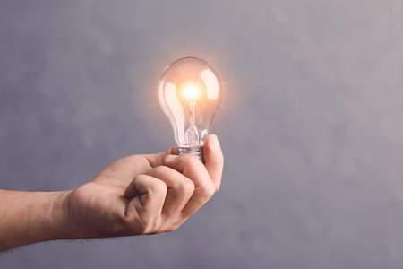 Businessman holding a clear light bulb with light effect on gray space wall background. Concept of new ideas for work.の写真素材