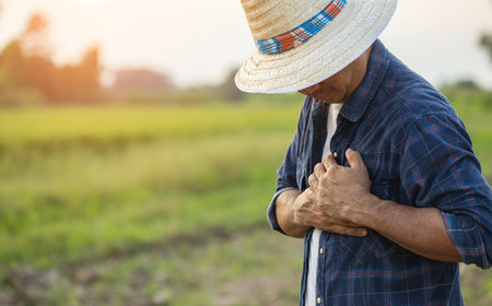injuries or Illnesses, that can happen to farmers while working. Man is using his hand to cover over left chest because of hurt,  pain or feeling ill. Health of agriculturist concept.の写真素材