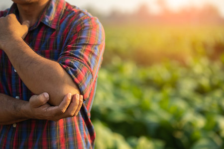Injuries or Illnesses, that can happen to farmers while working. Man is using his hand to cover over elbow because of hurt,  pain or feeling ill. Health of agriculturist concept.の写真素材