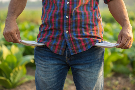 Empty budget, Lose profit, Fail, or unsuccessful in business concept. Asian farmer is standing in the tobacco field and showing empty trouser pocket. Financial problem in agriculture career concept.の写真素材