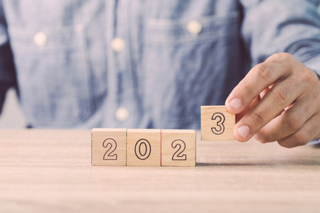 Businessman's hand is sorting out a wooden dice with the number of 2023 on the table. Work concept...