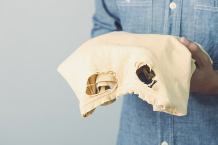 Used wrong type of washing powder concept. Man holding yellow torn and old T-Shirt. Studio shot on grey wall background.の写真素材