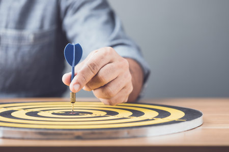 Start with new goal. Businessman working in the office and throwing arrow darts in the center of yellow dartboard. Goal and success for business concept.の写真素材