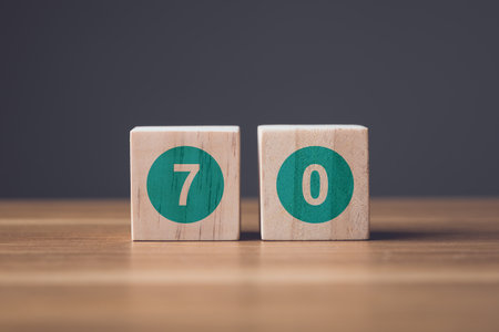 Number 70 write  on wooden blocks and arranged on wooden desk. Studio shot on grey backgroundの写真素材