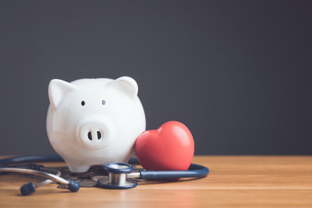Financial health check, The idea of ââsaving money for health care concept, Close up white piggy bank, stethoscope and red heart on wooden desk with grey copy space wall. Health and finance concept.の写真素材