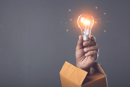 Creative new design thinking for work, Hand holding light bulb and old cardboard box on dark background, hand pops out of old cardboard box. Can use for reuse and recycle concept. Studio shot.の写真素材