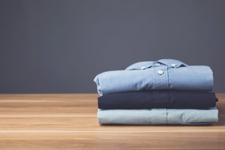 Close up stack of new color men shirt on wooden desk with dark space grey background. Mens fashion clothing concept.の写真素材