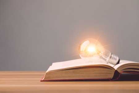 Close up clear light bulb with light effect on old book and put on wooden desk with grey space wall background. Idea of learning, Education concept.の写真素材