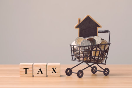 Tax for home and real estate payment concept. TAX write on wooden blocks arranged on top coin stack on office desk with grey wall background. Business, Financial ideas.の写真素材